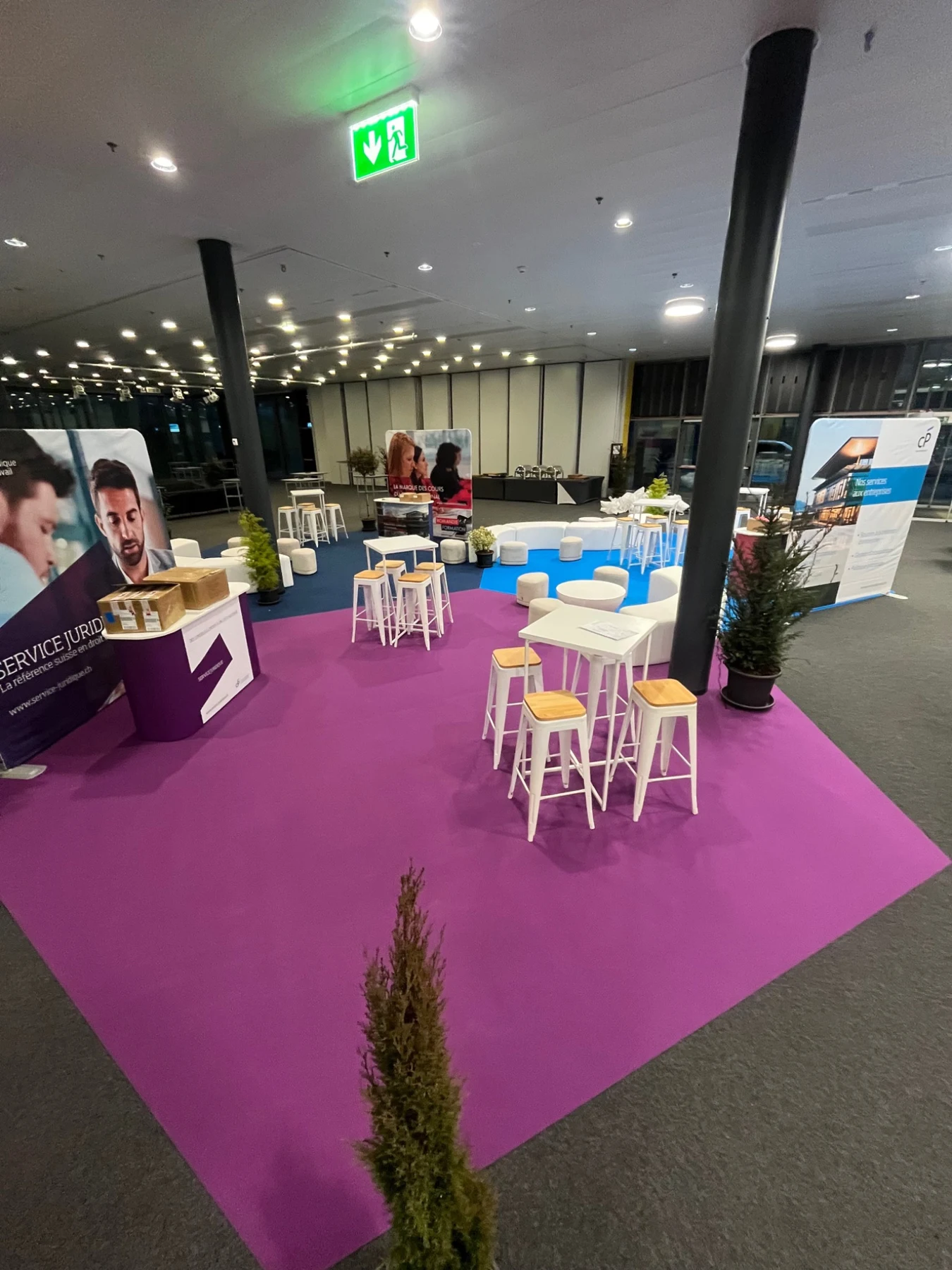 Espace de réception avec moquette violette, tables hautes et décoration végétale